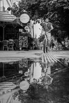 A man riding a bicycle reflects in a city street puddle, creating a striking urban scene.