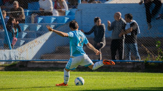 Soccer player kicks ball during game at Mendoza stadium, with spectators watching.