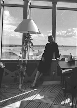Elegant caucasian woman in a black dress posing by the window in a stylish restaurant with a seaside view.