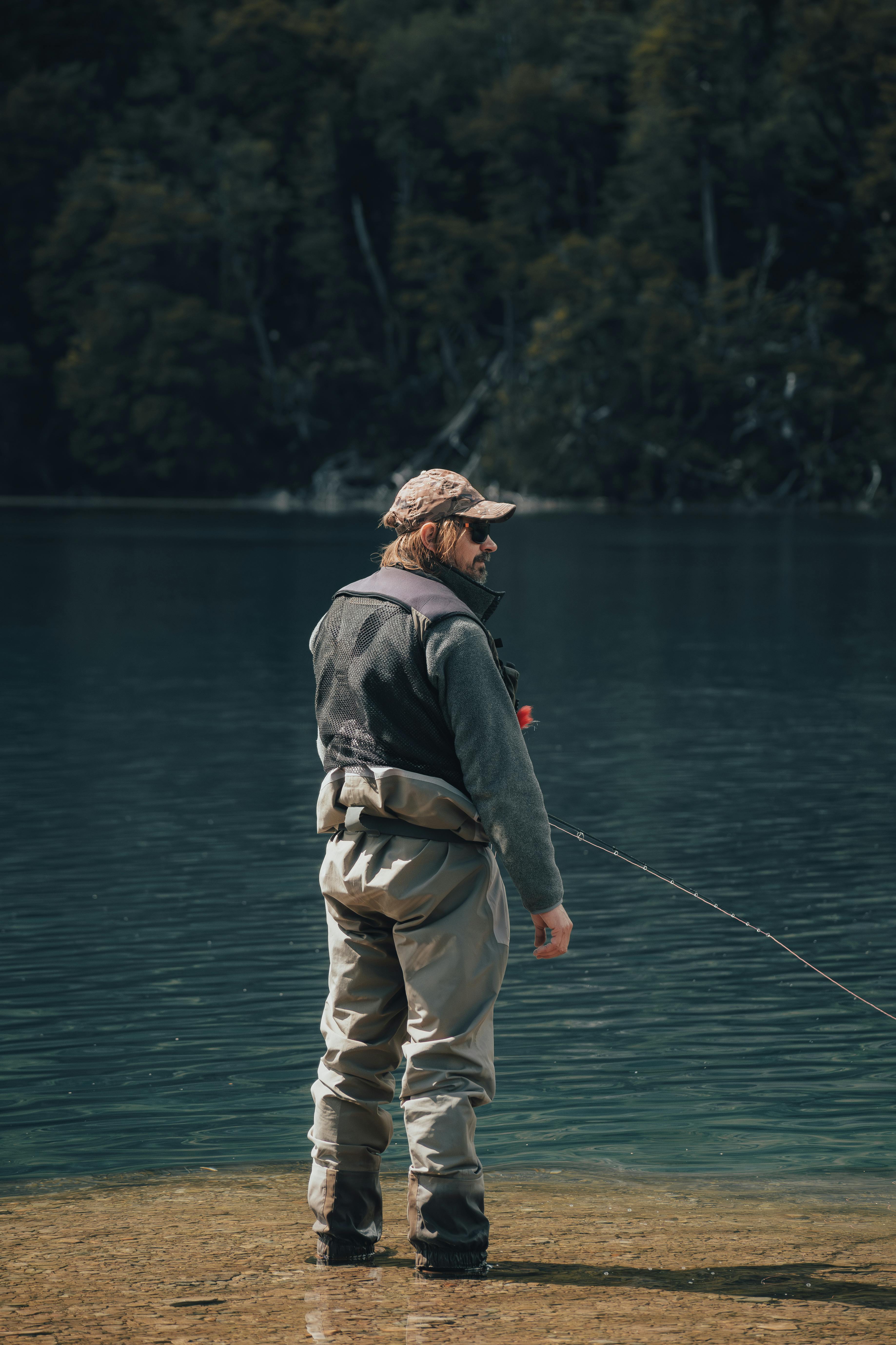 Adult man fishing in a serene lake, surrounded by lush wilderness.