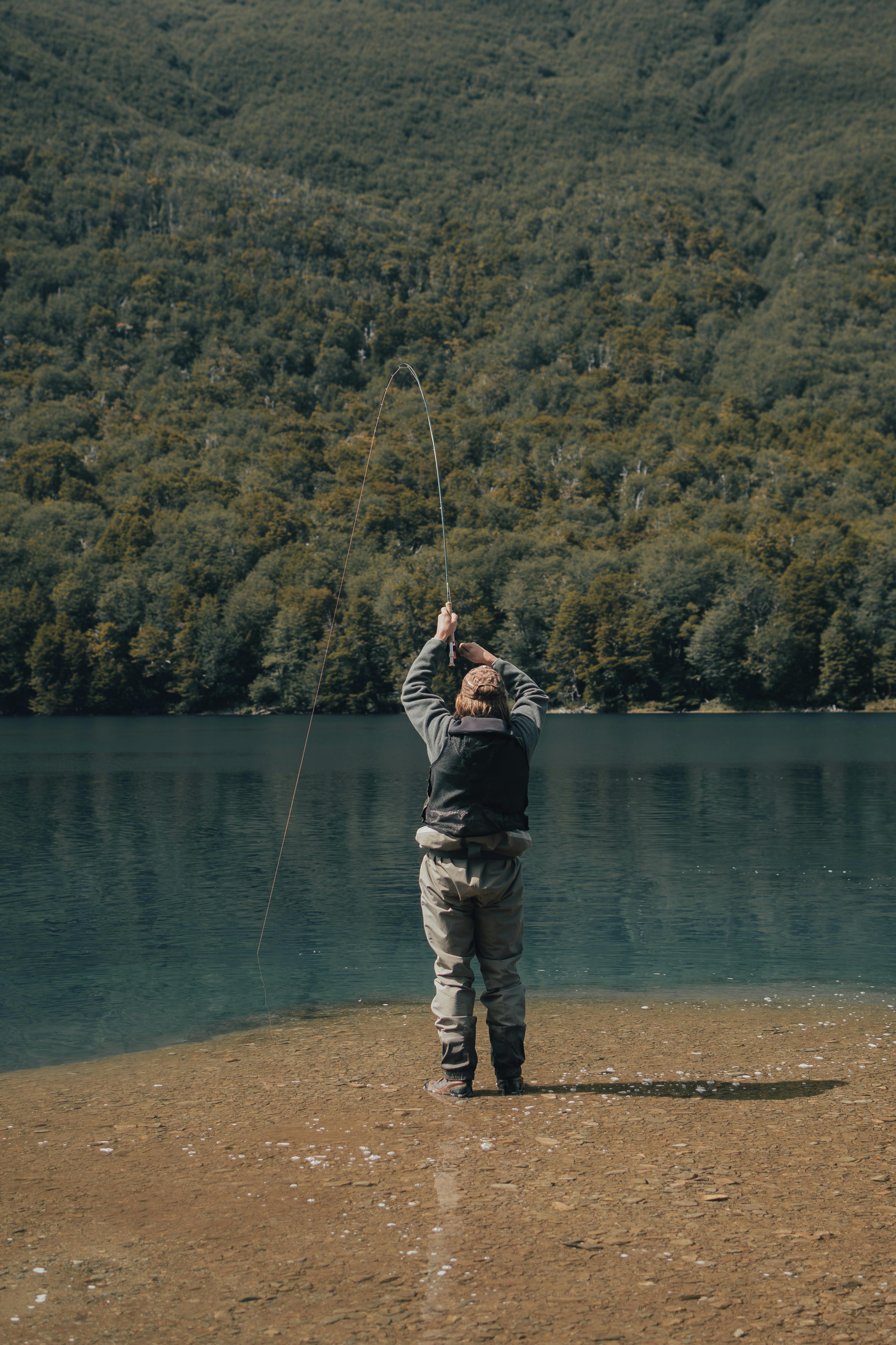 A man fly fishing in a tranquil mountain river surrounded by lush forests.