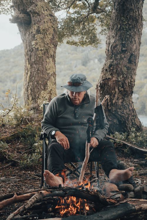 Free Man enjoys leisure time by a campfire in forest, provides tranquil wilderness vibe. Stock Photo