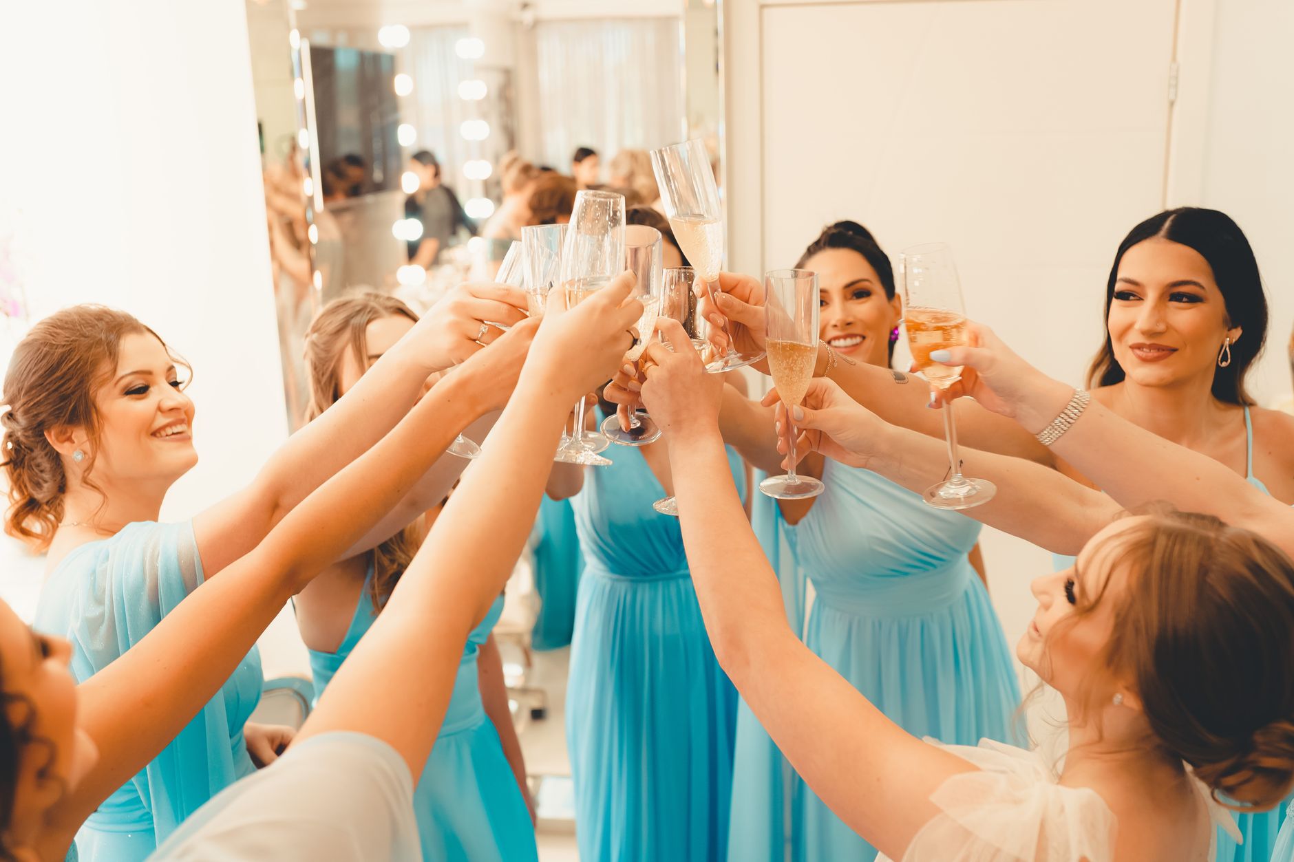 Bridesmaids in matching blue dresses raise champagne glasses for a celebratory wedding toast.