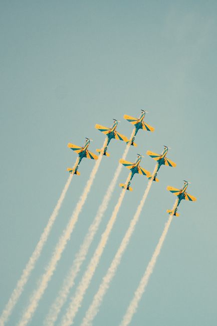 Vibrant aerobatic planes performing a precision airshow against a clear blue sky.