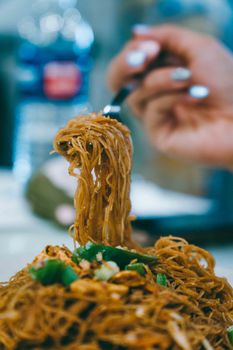Close-up of a hand with painted nails twirling stir-fried noodles on a fork in Kuala Lumpur.