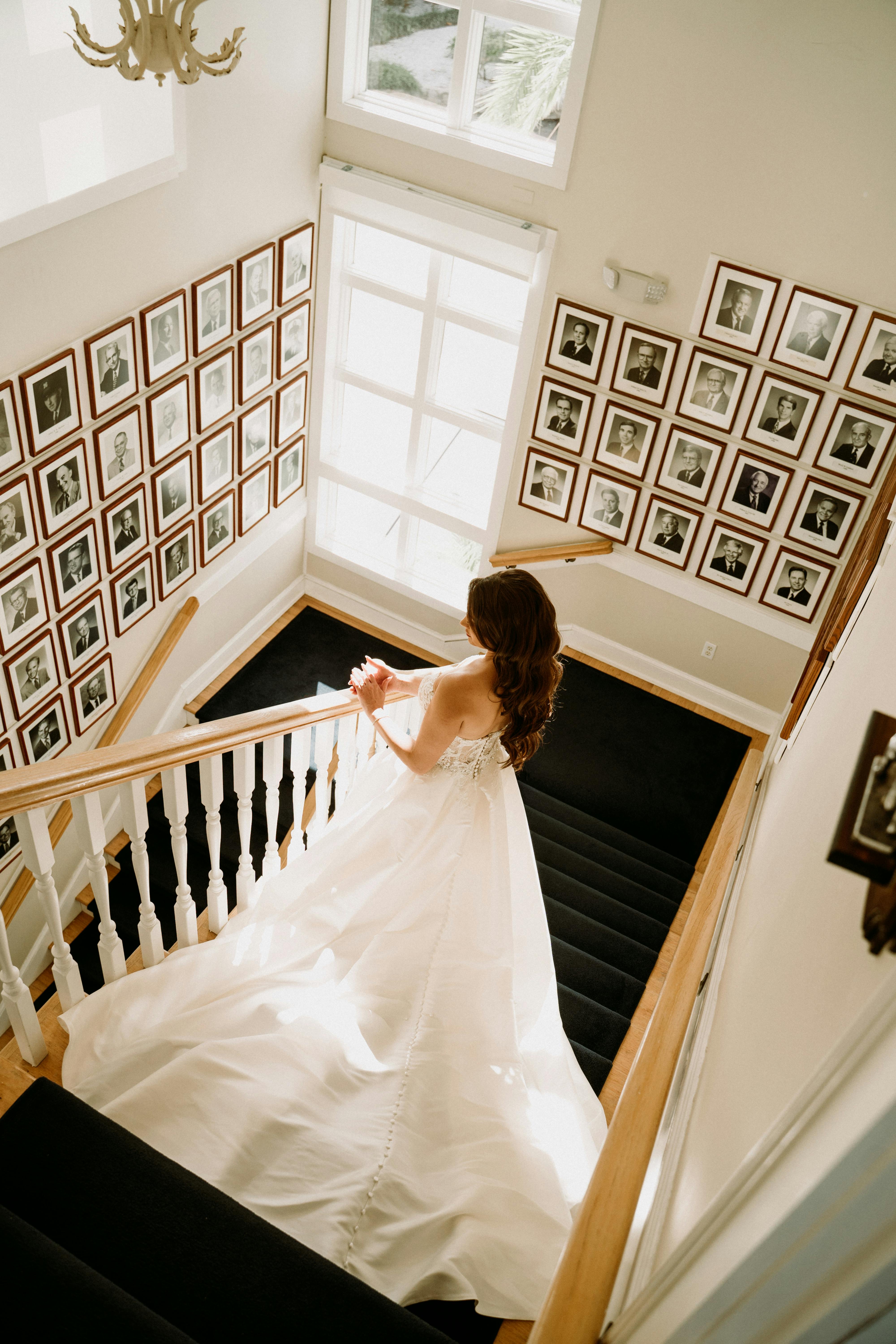 Brunette bride gracefully descending a staircase in a stunning wedding dress with gallery wall.