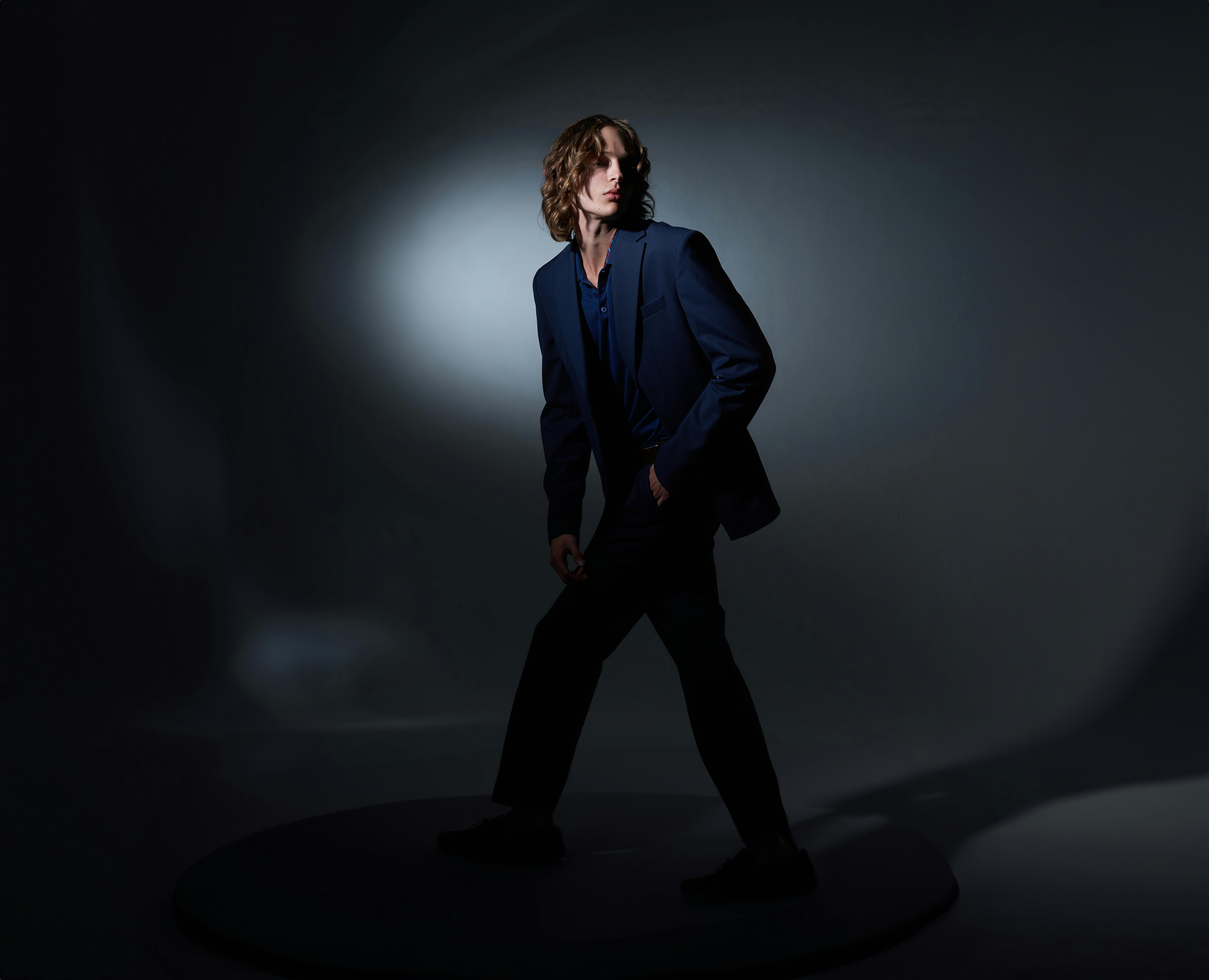A stylish man in a dark studio posing confidently under dramatic lighting.