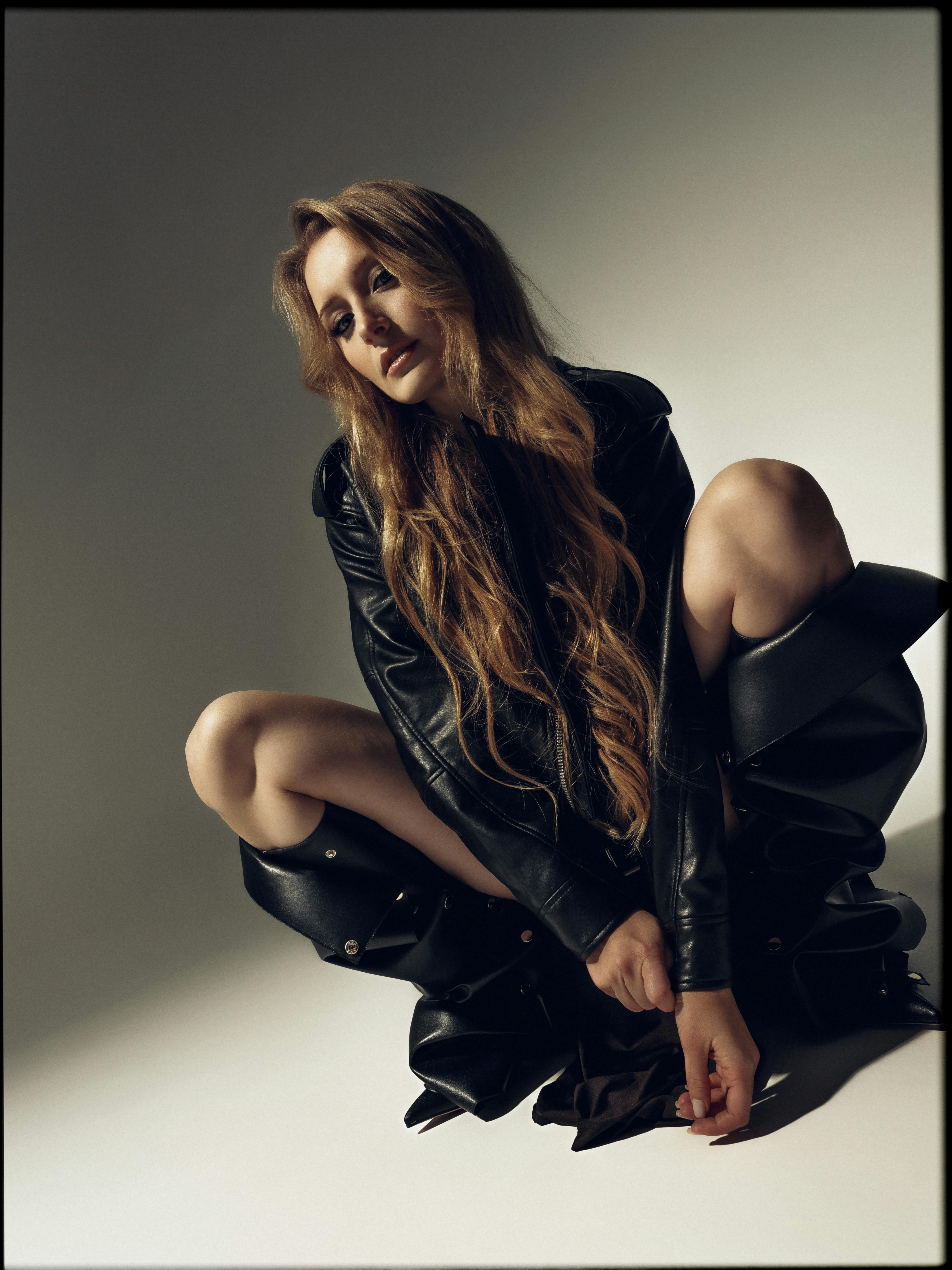 Woman with long hair posing in black leather outfit, studio shoot.