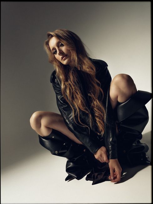 Woman with long hair posing in black leather outfit, studio shoot.