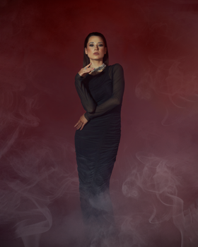Model in black dress posing elegantly with red background and smoke effect.
