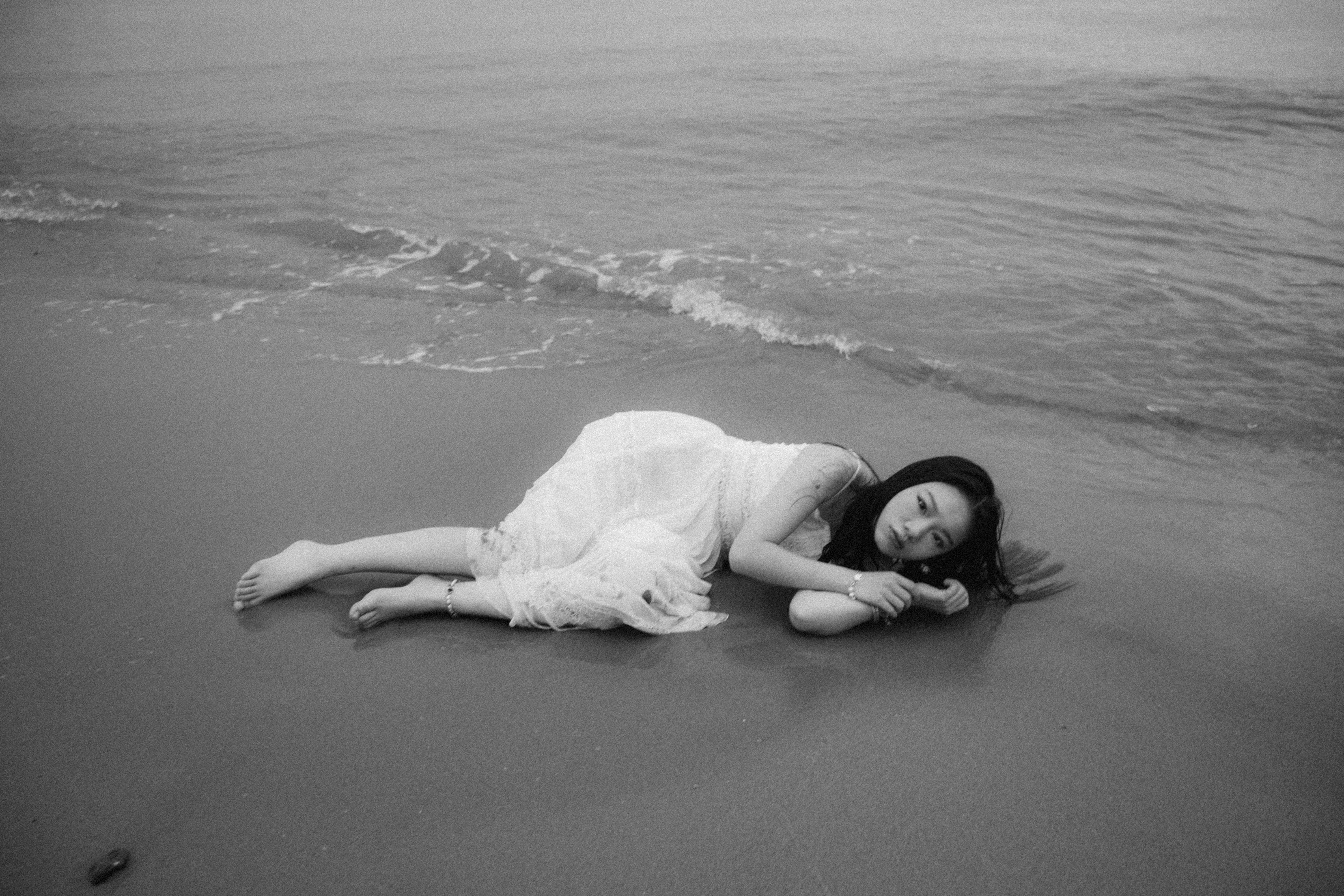 Young woman lying on a tranquil shore in a black-and-white beach portrait.