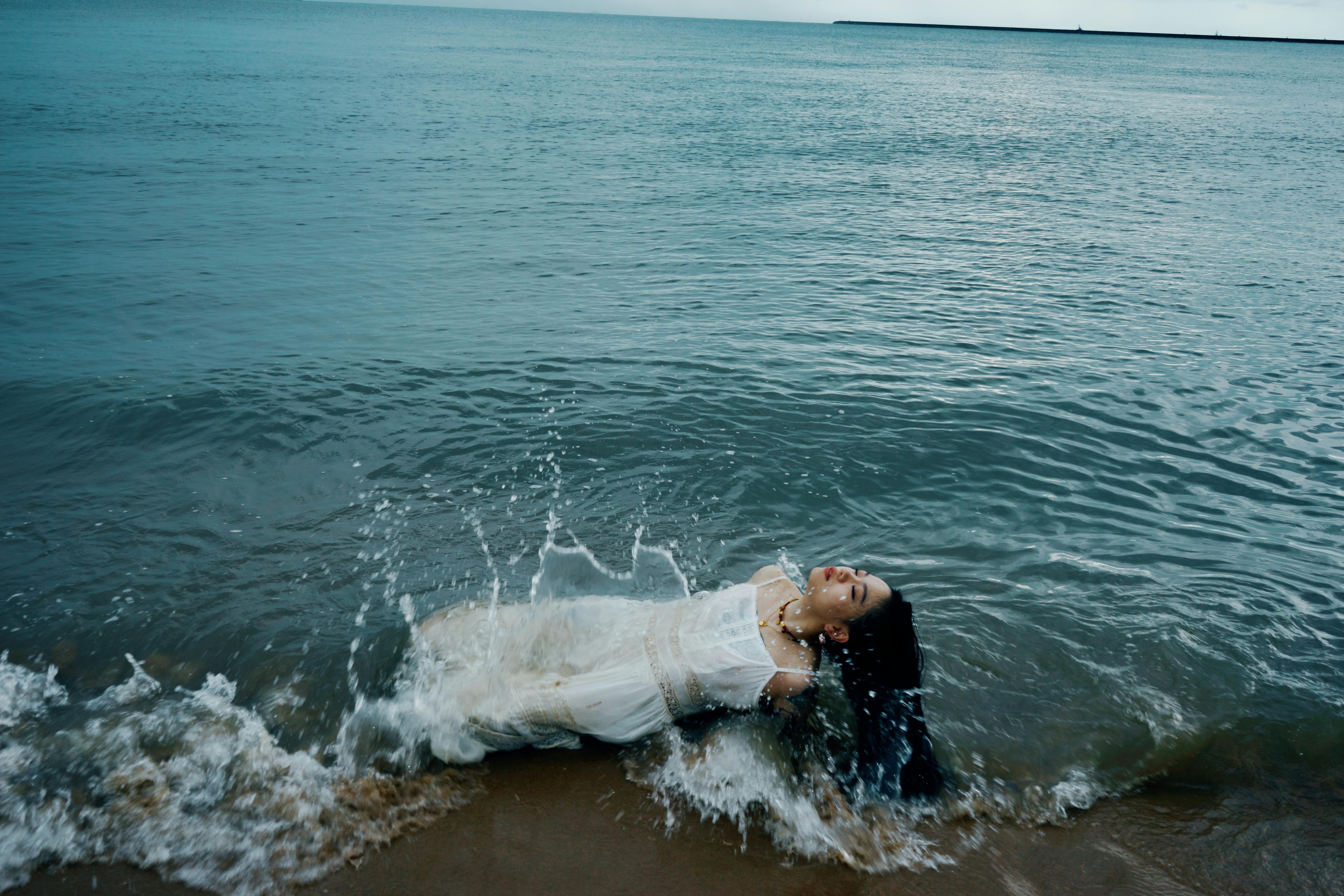 Woman in a white dress enjoys the ocean waves at the beach.