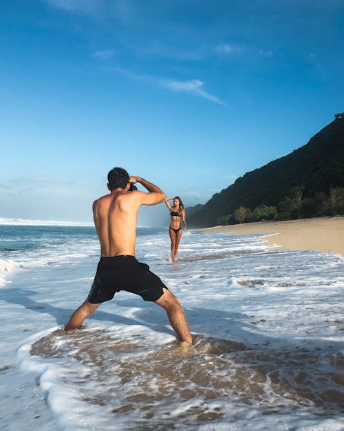 Gratis Pria Mengambil Foto Wanita Berdiri Di Pantai Foto Stok