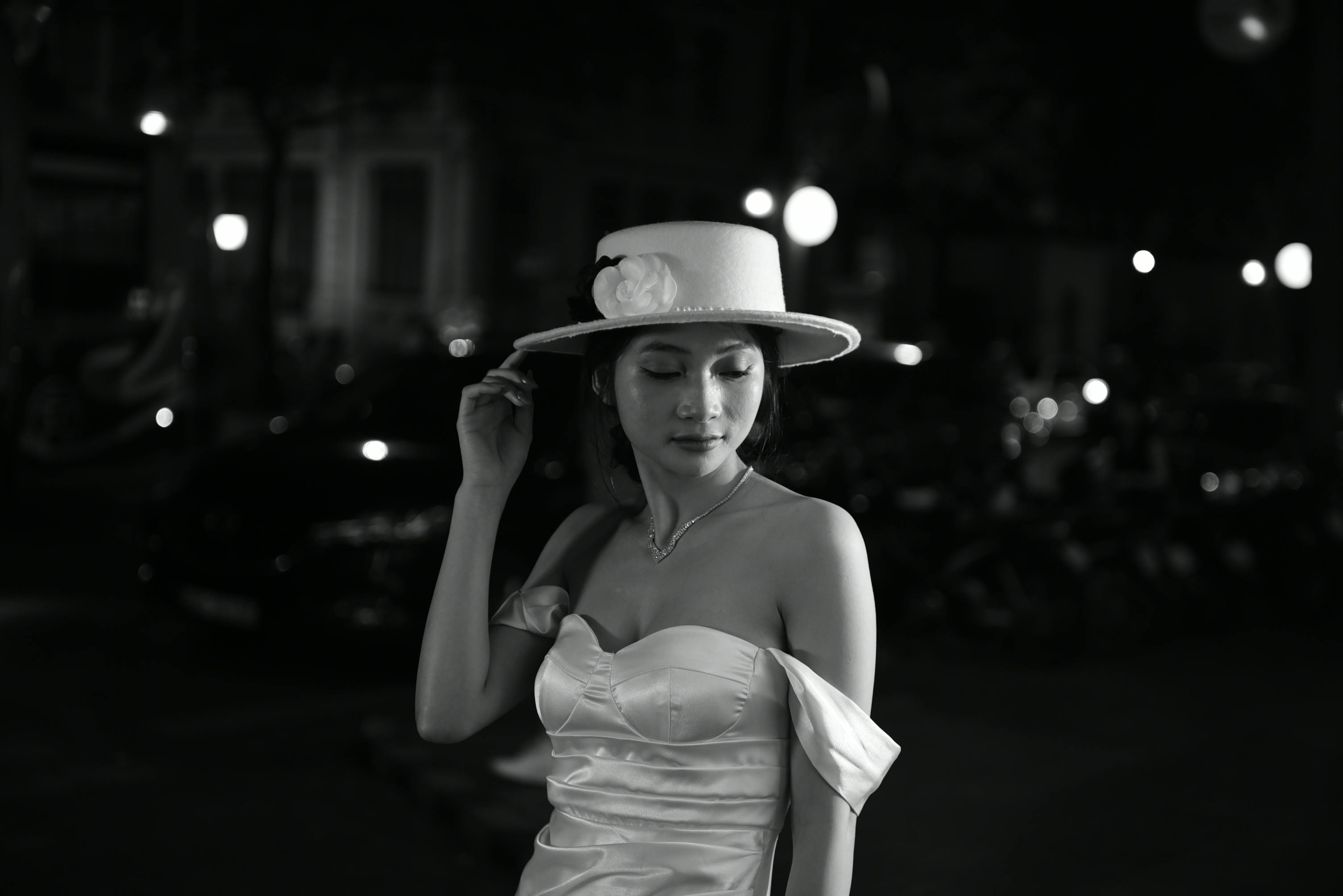 an elegant woman in a dress and a hat standing outside at night