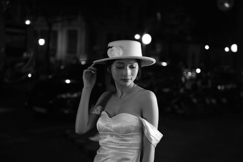 Free Black and white photo of a stylish woman wearing a white dress and hat at night. Stock Photo