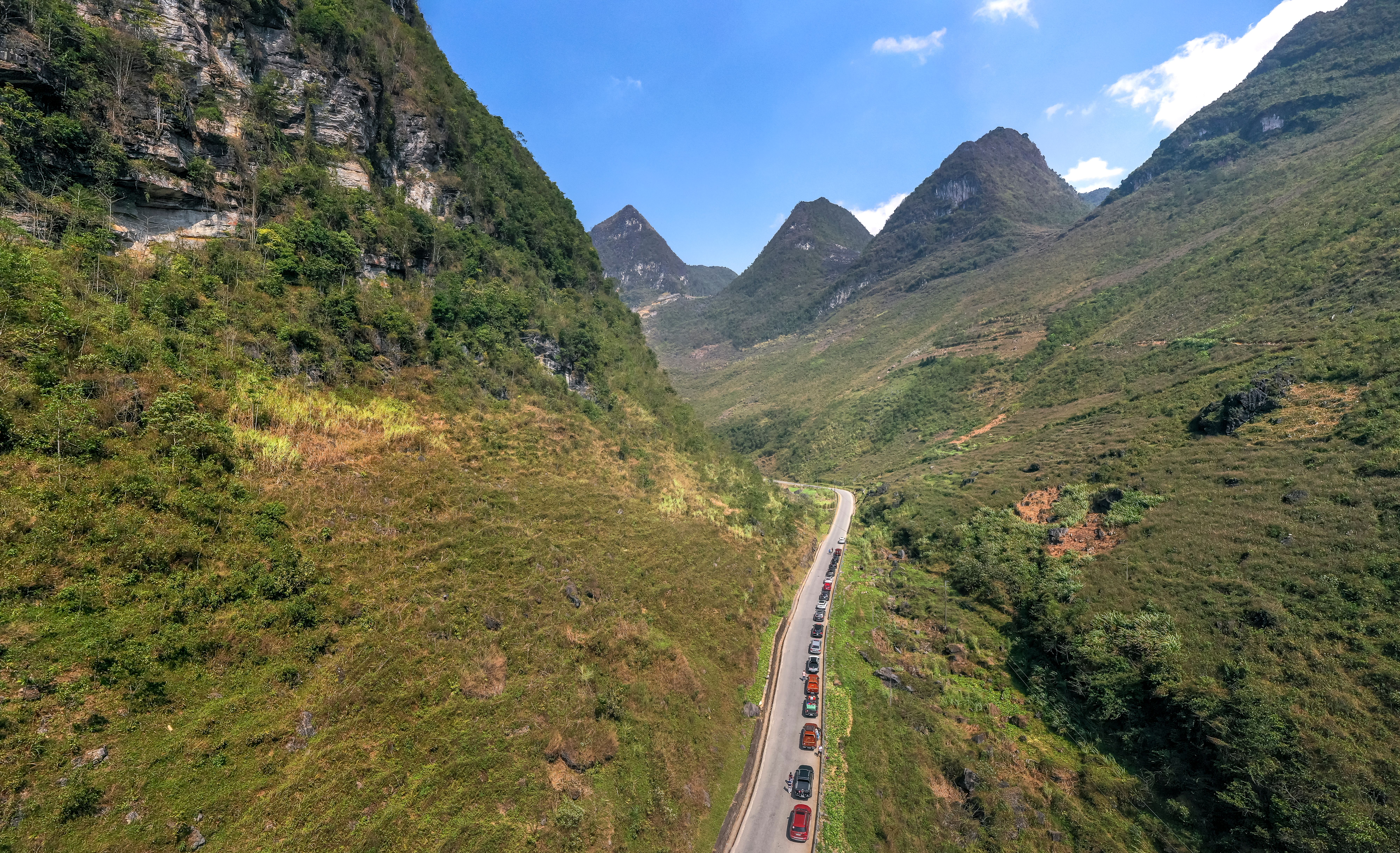 Aerial view of a picturesque mountain road winding through lush green valleys under a clear blue sky.