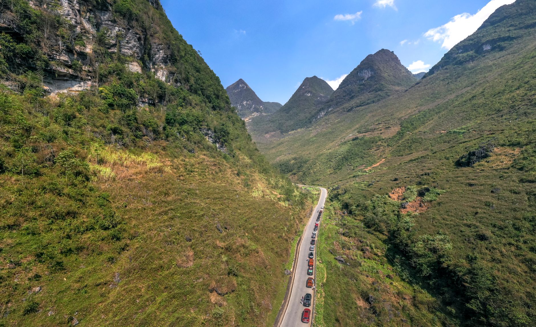 Aerial view of a picturesque mountain road winding through lush green valleys under a clear blue sky.