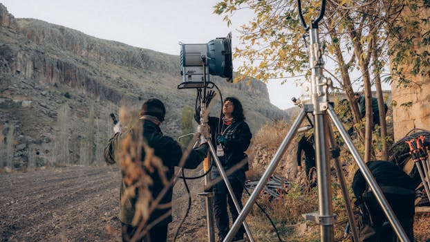 Film crew preparing lighting equipment in a rugged rural landscape.