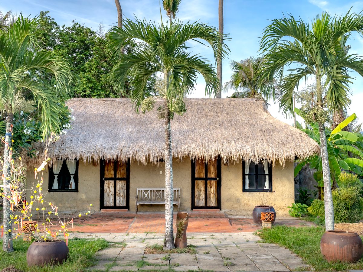 A thatched tropical cottage surrounded by palms and greenery