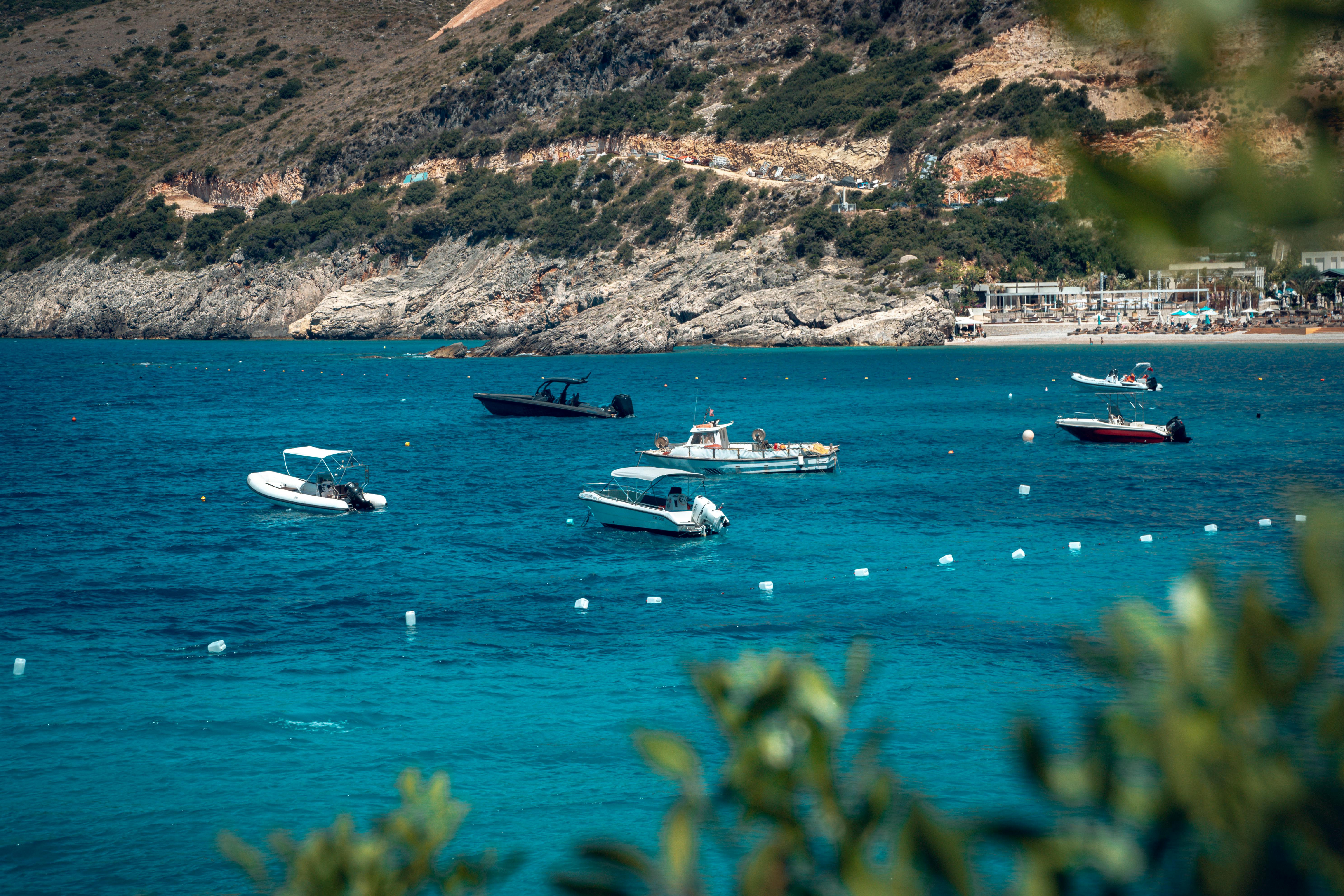 A beautiful summer day in Jala Bay, Albania, showcasing boats on turquoise waters against rugged cliffs.