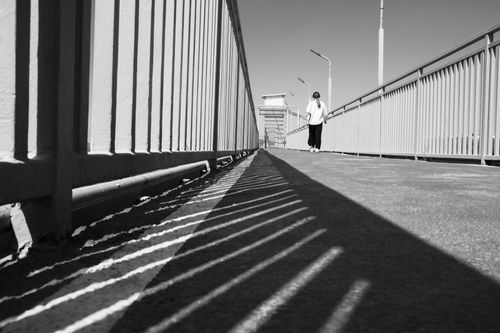 Free A woman walks alone on a shadow-lined footbridge in an urban setting. Stock Photo