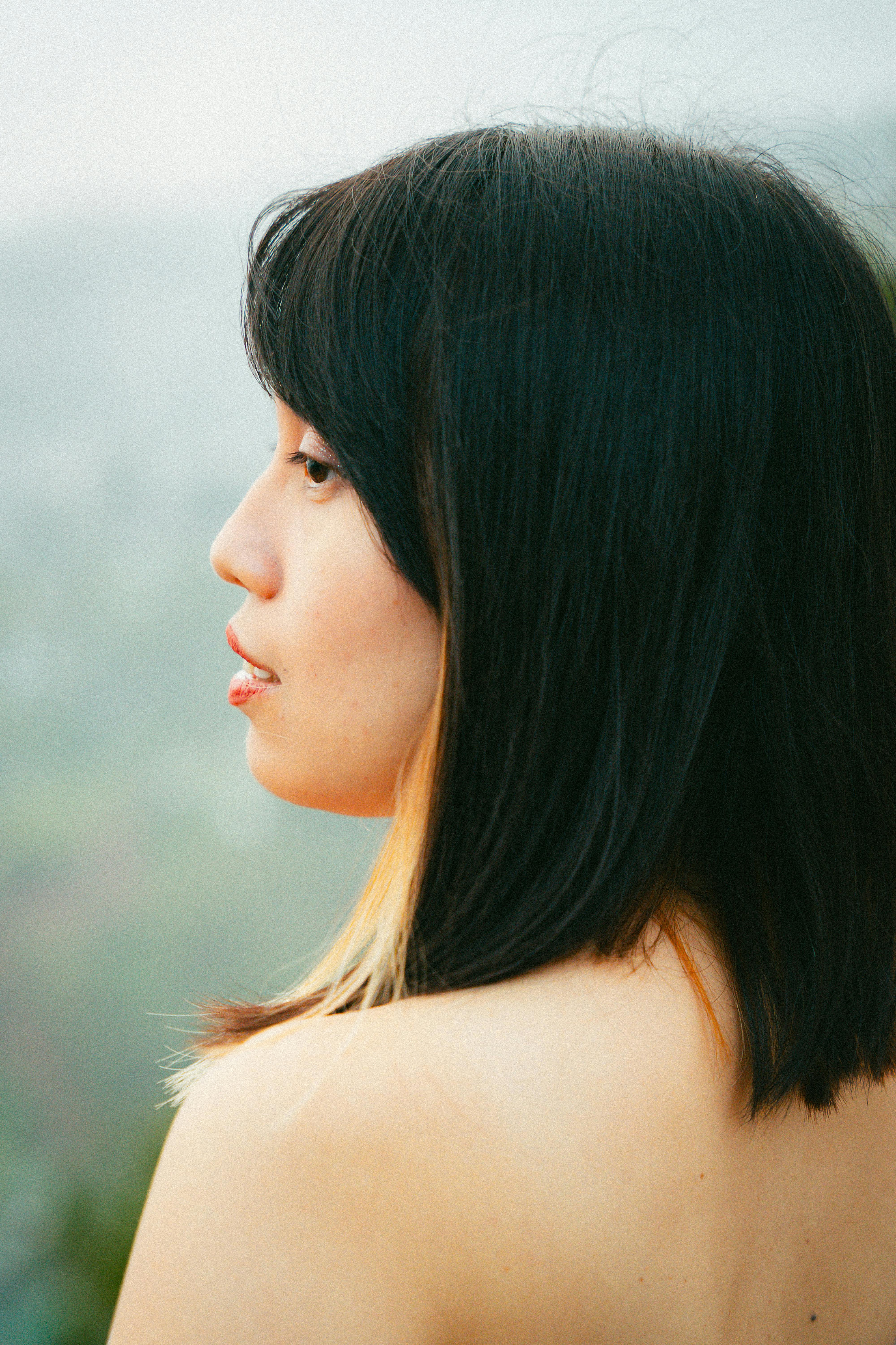 A tranquil side profile of a young woman with blurred natural background.