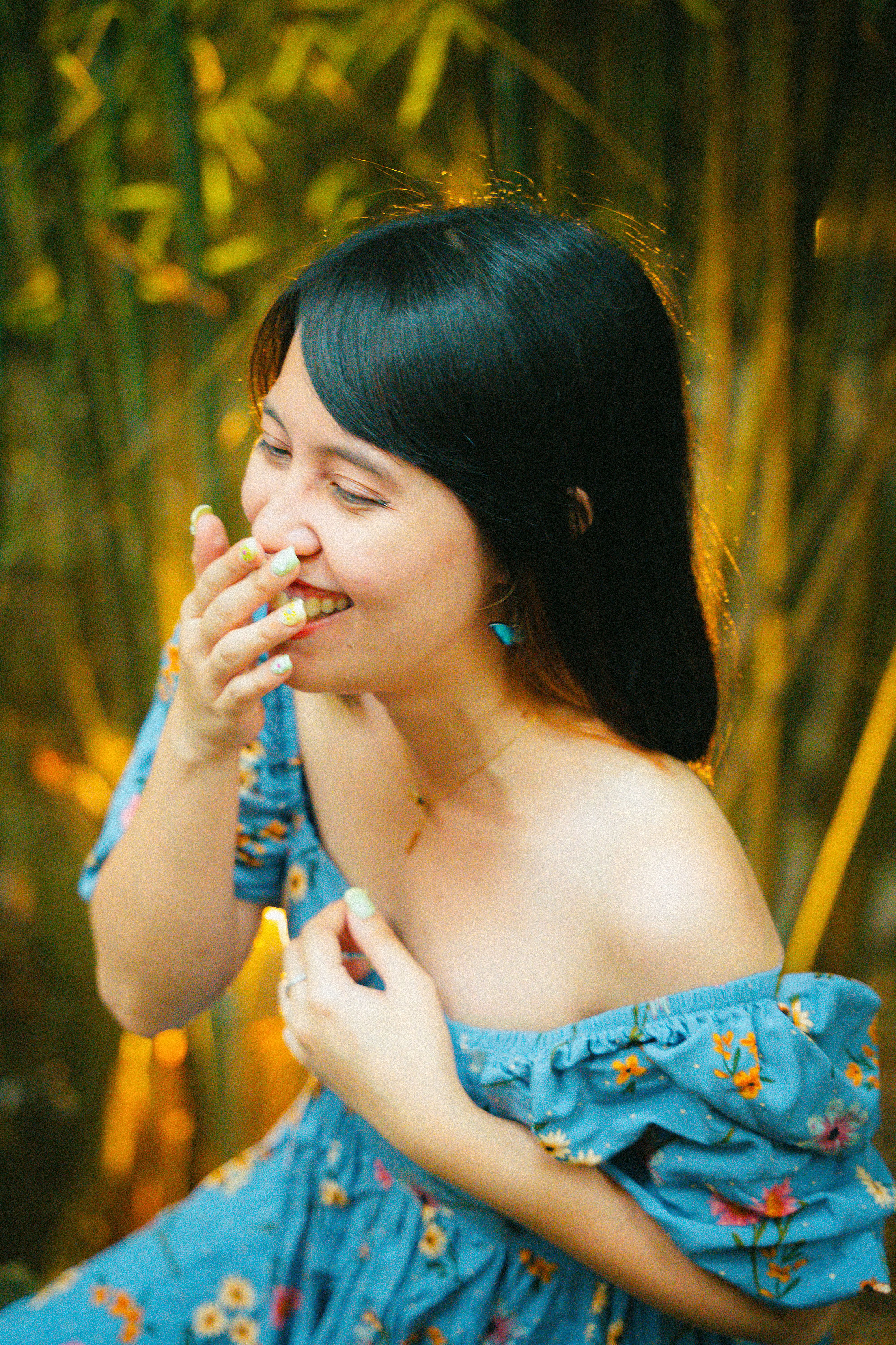 Delightful portrait of an Asian woman laughing while outdoors in a sunlit garden.