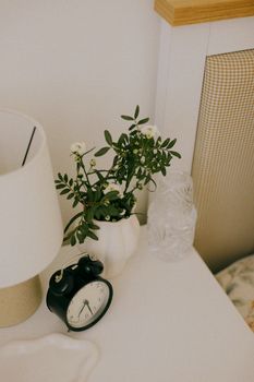 Chic nightstand featuring a classic alarm clock, vase with flowers, and lamp for a cozy ambiance.