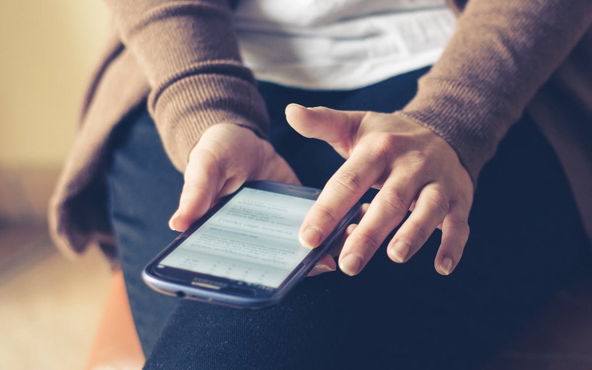 Free Person Holding Smartphone While Sitting Stock Photo