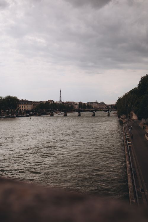 Free Scenic view of the Eiffel Tower and bridge across the Seine River in Paris under cloudy skies. Stock Photo