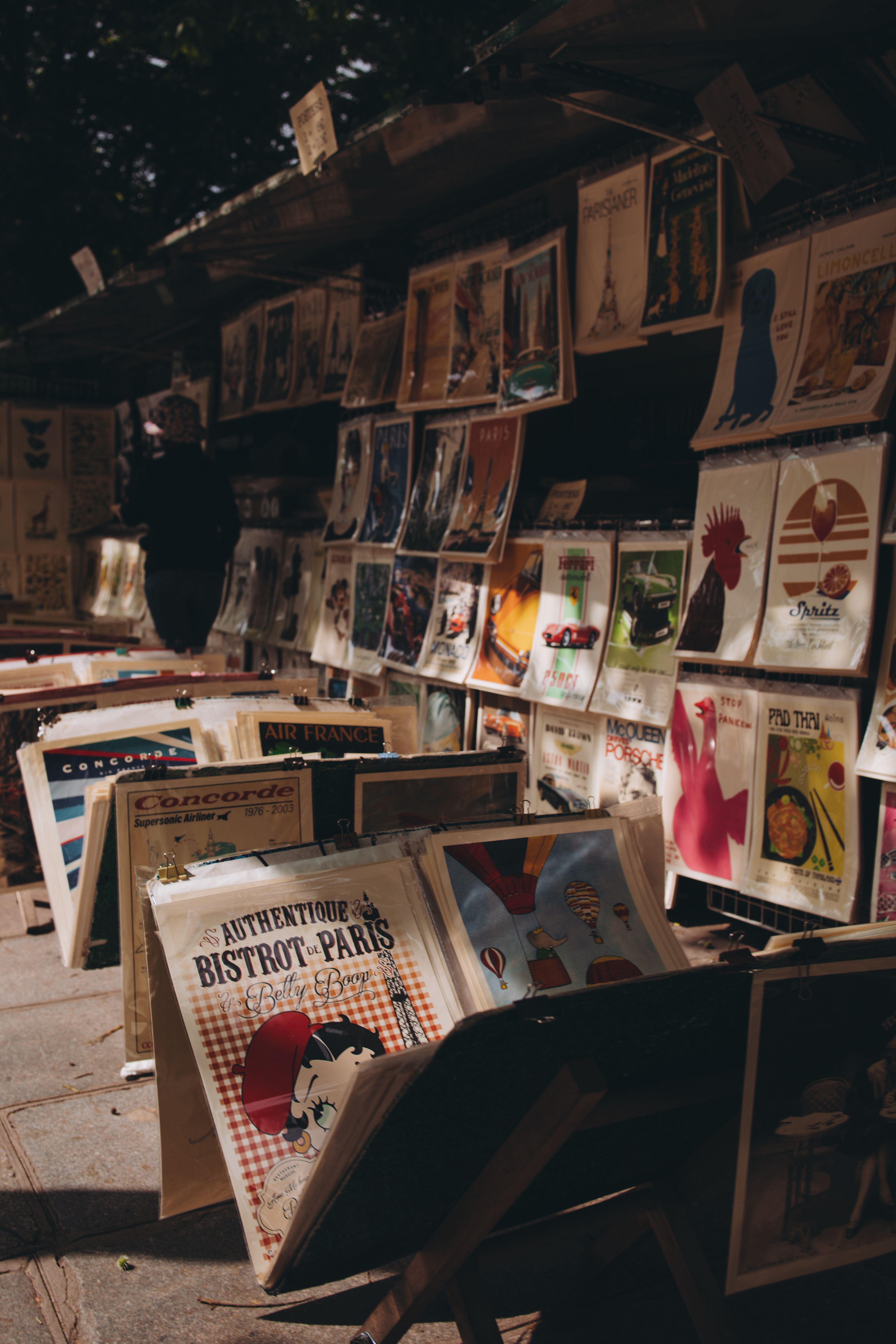 A collection of vintage posters displayed on a city street stall under the shade.