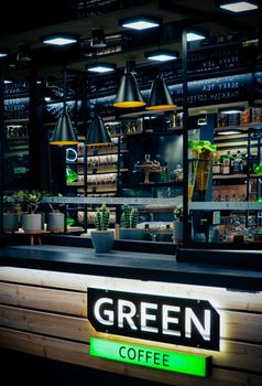 Contemporary coffee shop interior featuring green decor, potted plants, and industrial lighting.