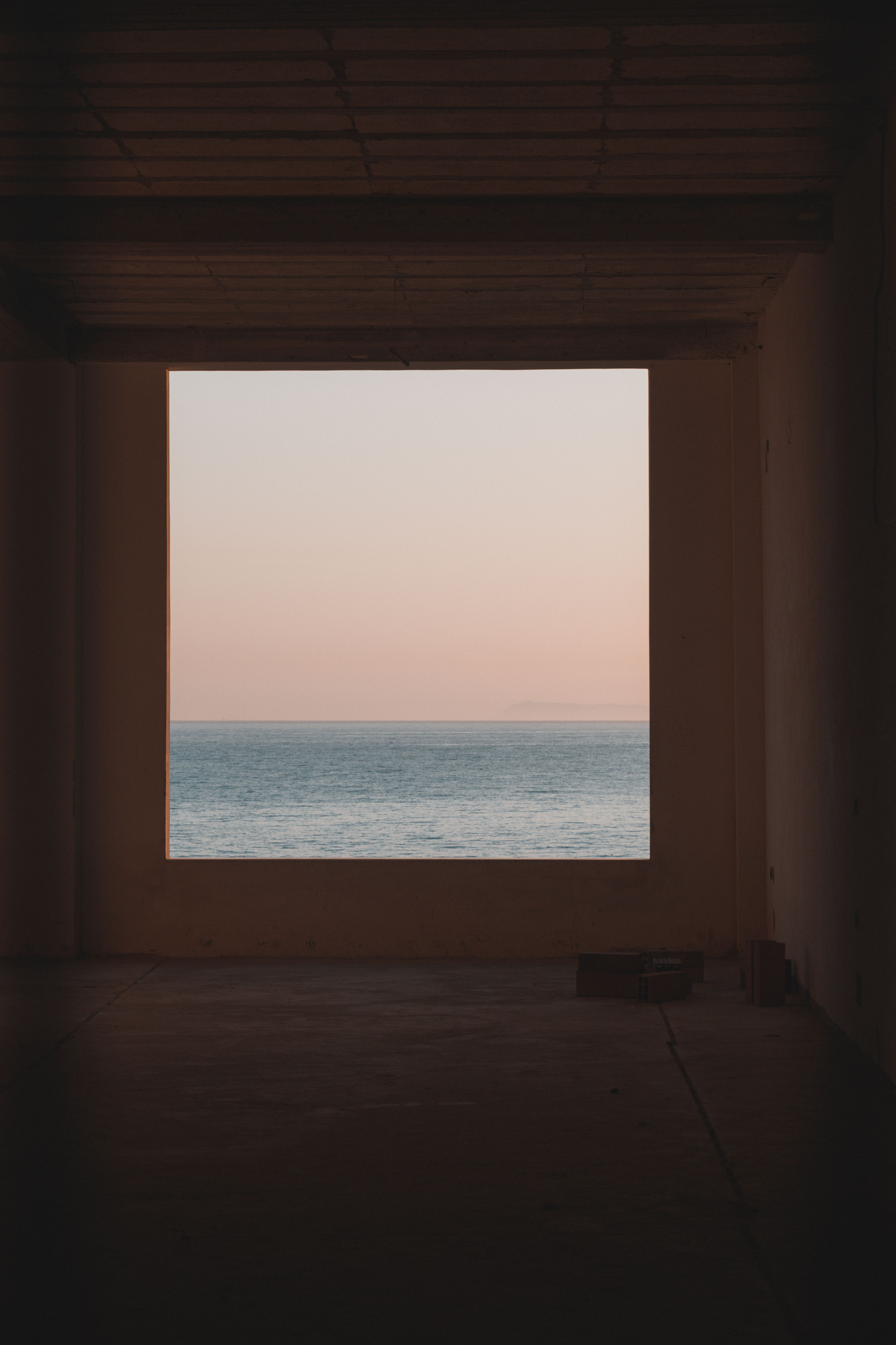 Free A serene view of the sea through a window frame at sunset, showcasing the tranquil beauty of Sarandë, Albania. Stock Photo