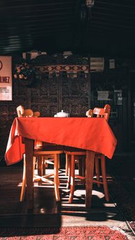 A warm, inviting restaurant interior featuring a sunlit table with a red tablecloth.