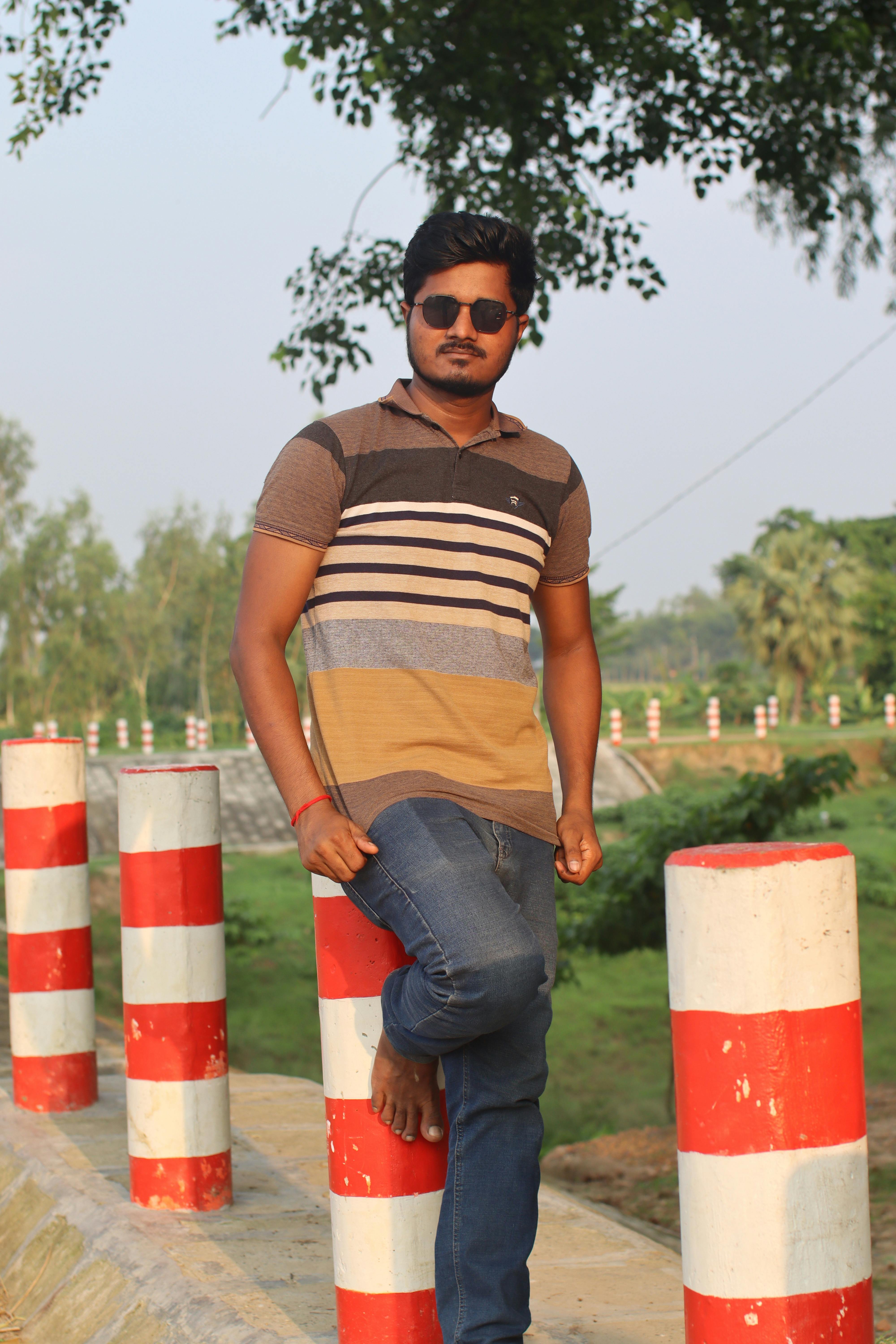 Casual portrait of a man in sunglasses, leaning on bollards in a sunny outdoor setting.