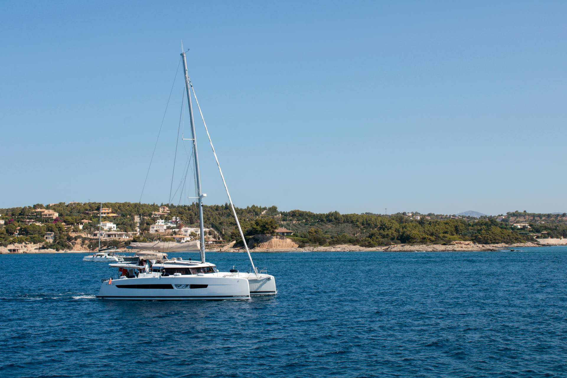 Serene yacht sailing near the picturesque coastline of Idra, Greece, under a clear summer sky.