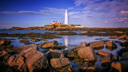 A lighthouse sits on a rocky shore with water and rocks