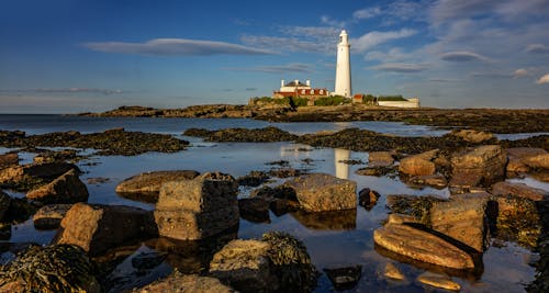 A lighthouse sits on a rocky shore with water and rocks