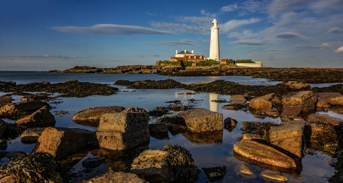 Free Breathtaking view of a lighthouse on rocky coastline during daylight reflecting in calm sea. Stock Photo