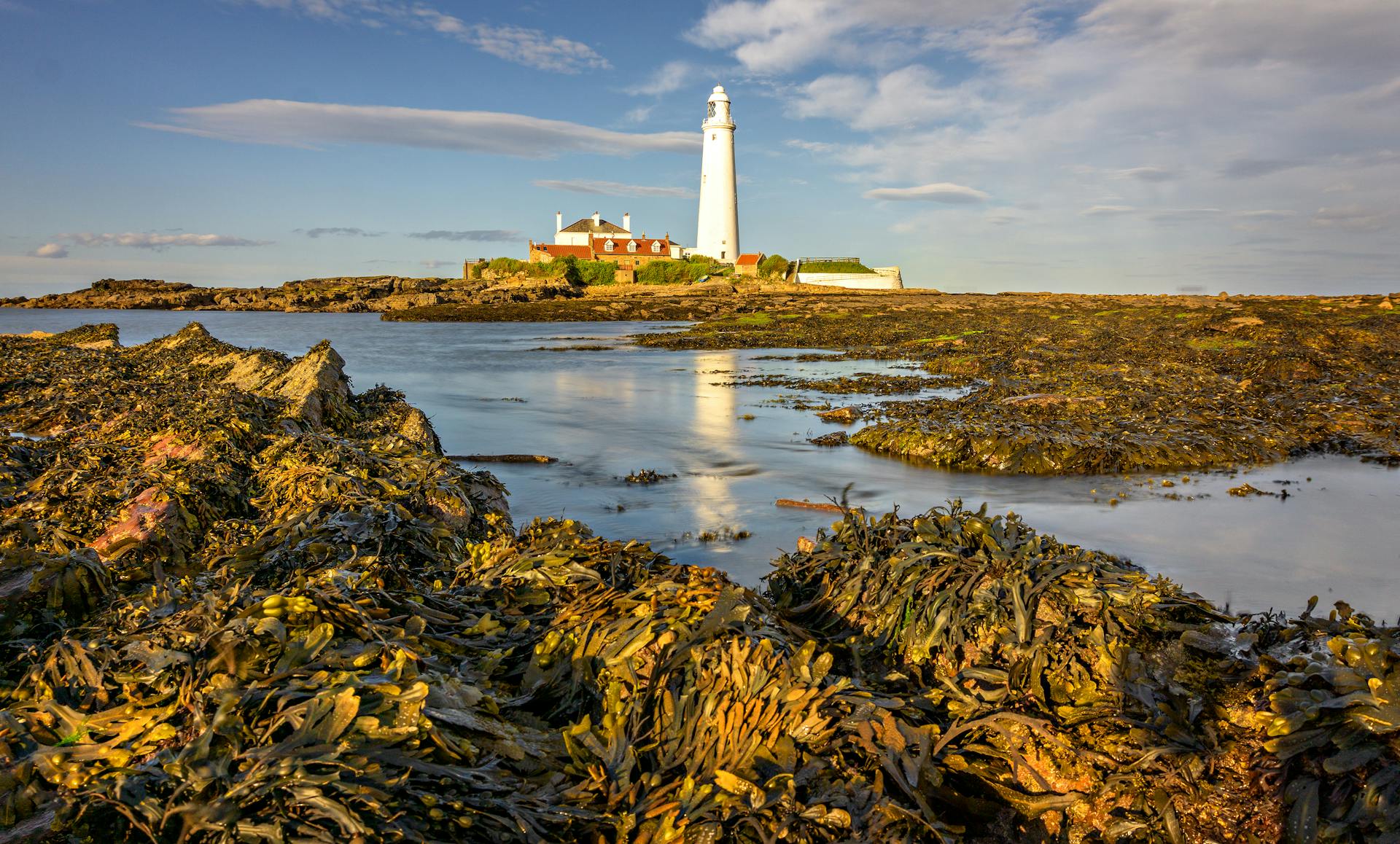 A picturesque lighthouse at sunset on a rocky coastline, surrounded by calm seas.