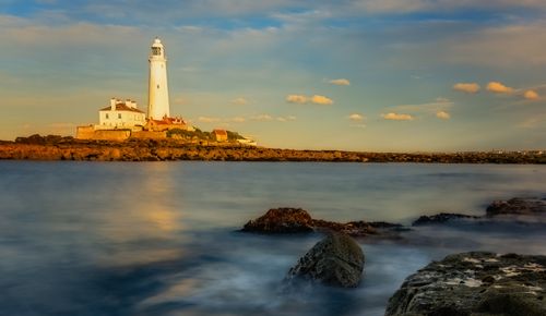 Free Stunning sunset view of St Mary's Lighthouse with calm sea and rocks in foreground. Stock Photo
