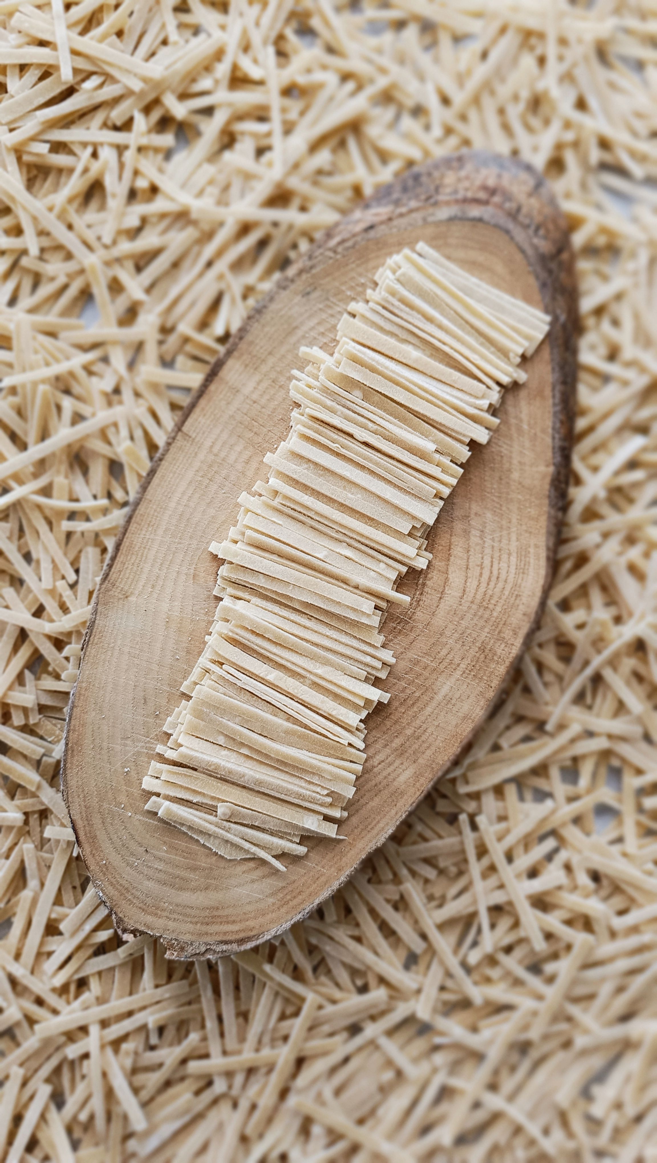 Top view of neatly stacked dry noodles on a wooden platter against a background of more noodles.