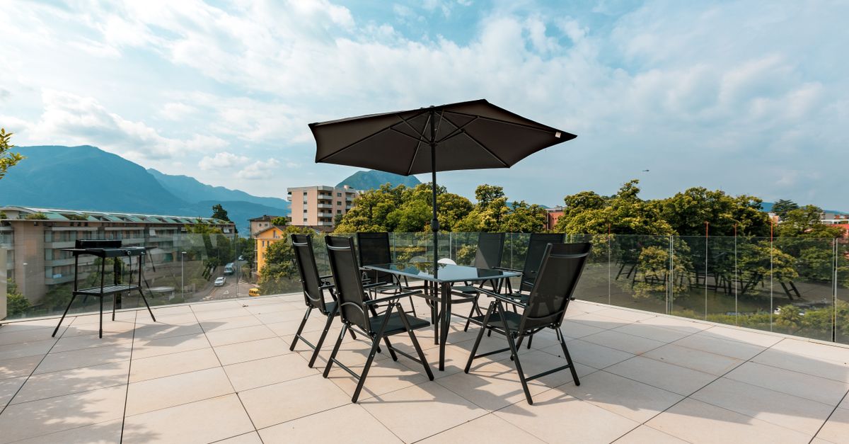 Spacious patio with seating and umbrella overlooking mountains and cityscape.