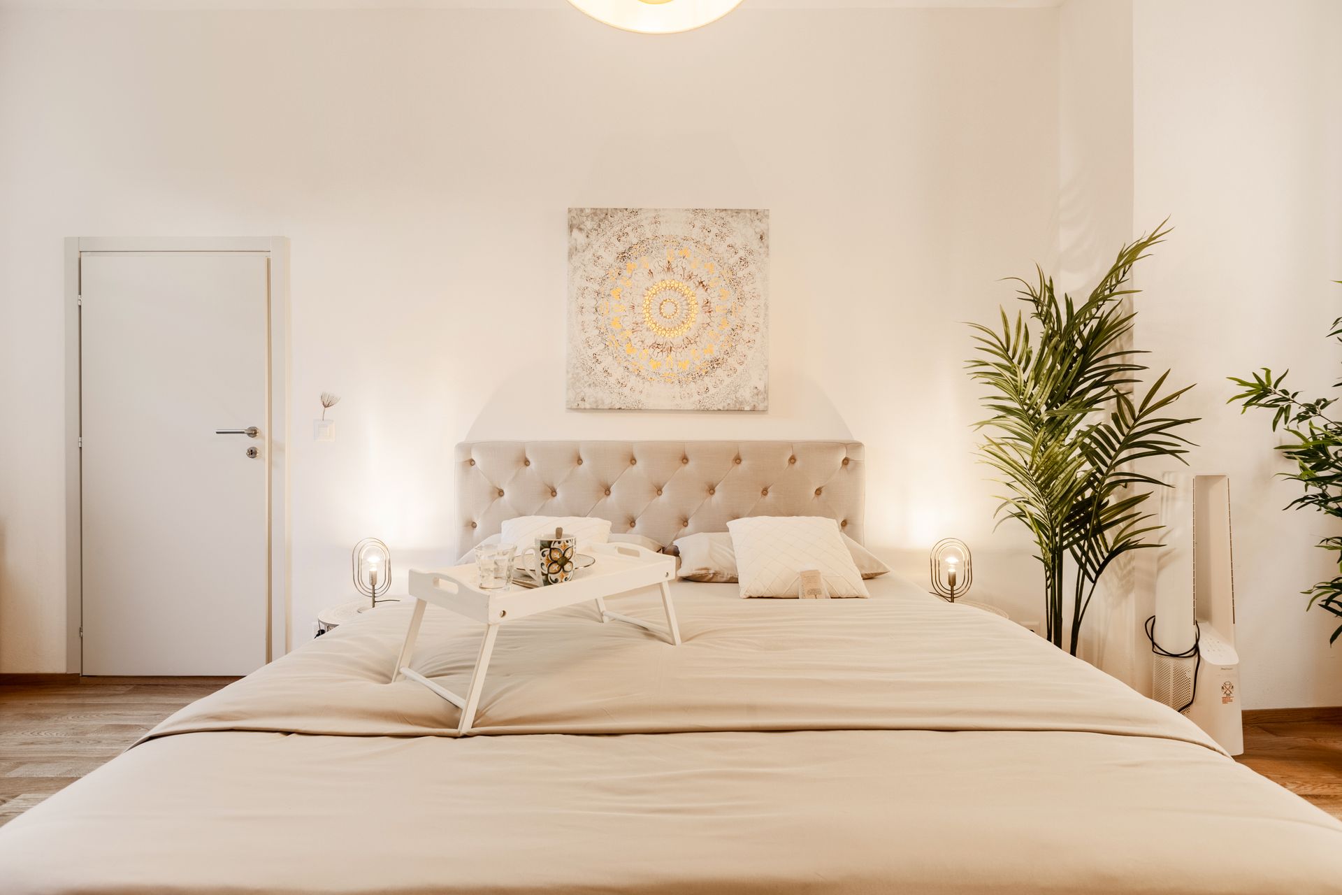 Elegant bedroom features a comfortable double bed with a breakfast tray against a backdrop of lush plants.