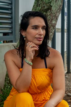 A thoughtful woman in a yellow dress sits outdoors, offering a serene summer portrait.