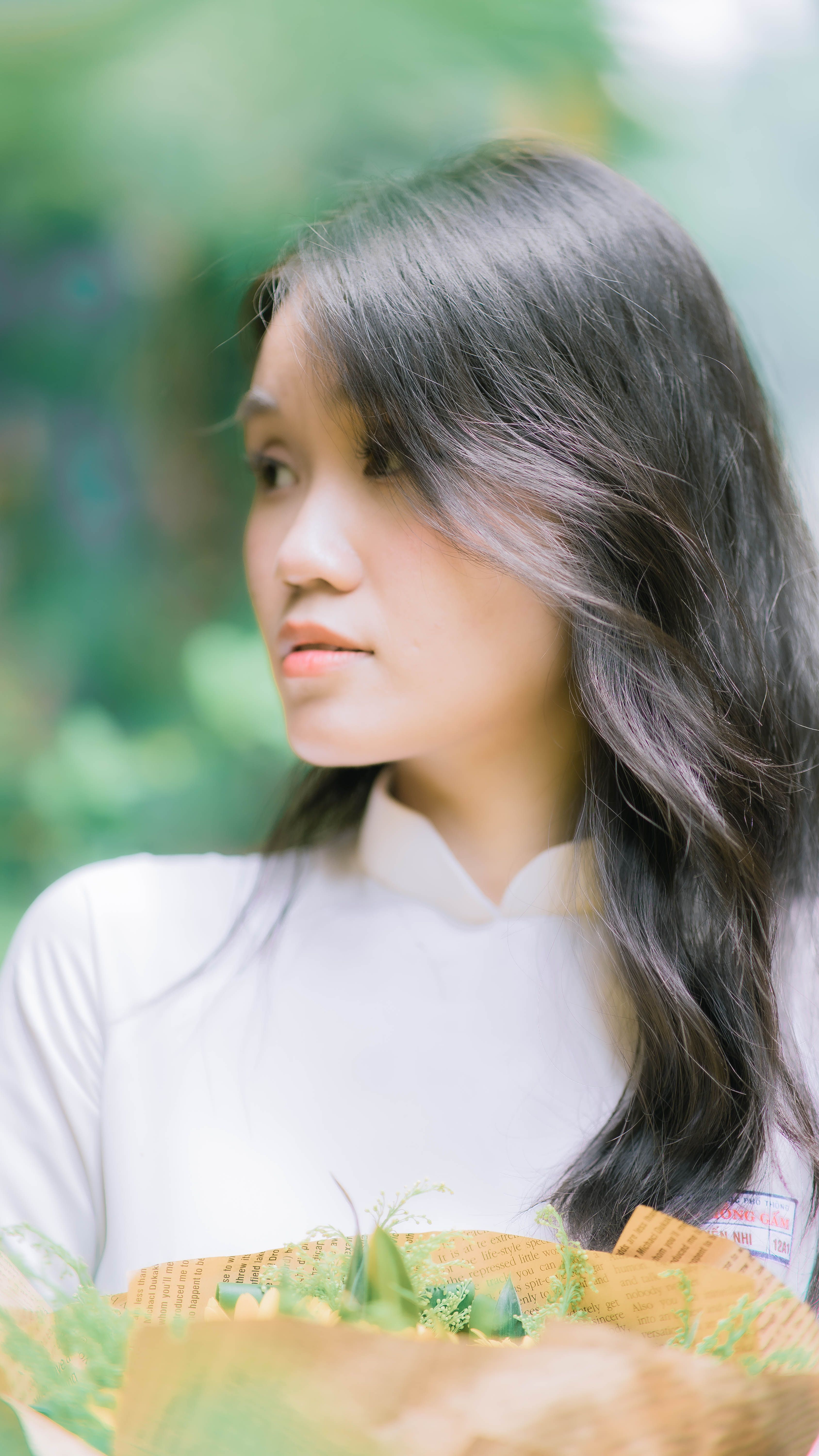 A portrait of an Asian woman with long black hair holding a bouquet in soft natural light.