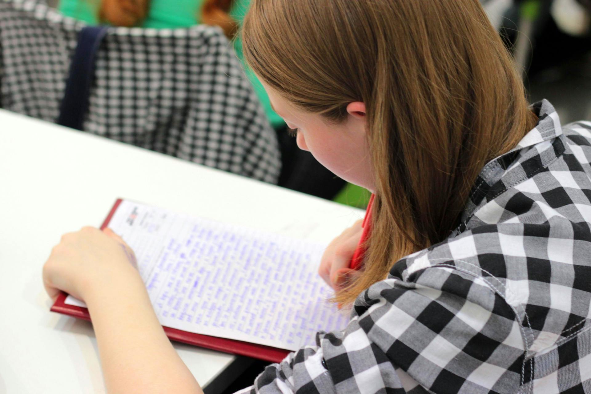 A young student writing in a notebook during a study session indoors.