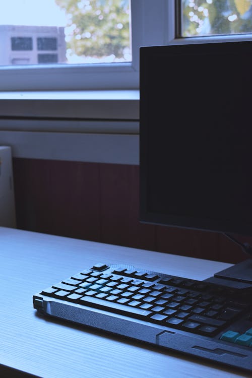 窓際の木製の机の上のデスクトップモニターとキーボードのクローズアップ写真