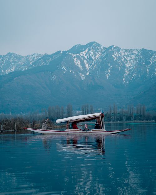 Free A peaceful traditional boat journey on Dal Lake with snow-capped mountains in the background. Stock Photo