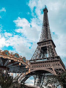 Eiffel Tower in Paris with carousel in foreground under a bright blue sky.